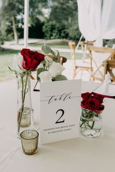 two vases with roses are sitting on a table at a wedding reception in front of an outdoor tent