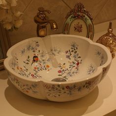 a white sink with flowers painted on it and gold faucets in the background