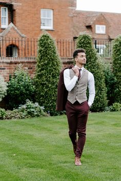 a man walking across a lush green field next to a tall brick building with ivy growing on it's sides