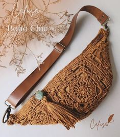 a crocheted purse with a leather strap and tassels on the bottom