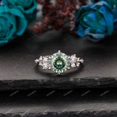 an engagement ring with green and white diamonds on it, surrounded by flowers in the background