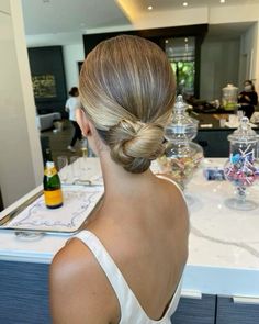 a woman sitting at a table in front of a counter with bottles and glasses on it