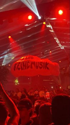 a large group of people in a room with red lights and some signs on the ceiling