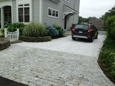 a car is parked in front of a house with gravel driveway and landscaping around it