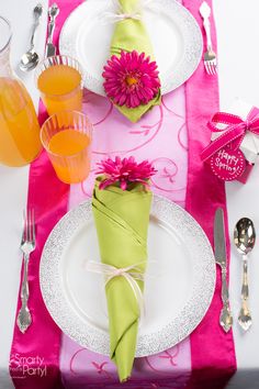 the table is set with pink and green napkins, silverware, and flowers