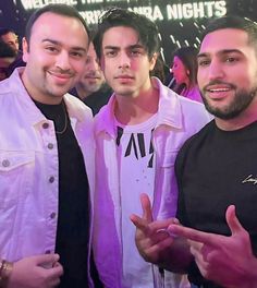 three men standing next to each other in front of a neon sign that says we are the night