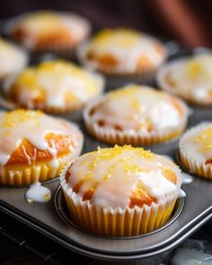 cupcakes with white icing and orange glaze sitting in a muffin tin