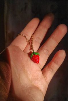 a hand holding a tiny strawberry necklace on it's thumb, with a chain around it