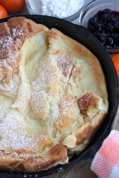 a skillet filled with fruit and powdered sugar on top of a wooden table