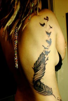 a woman's back with a feather tattoo on it