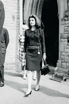 black and white photograph of woman walking in front of building with man standing next to her