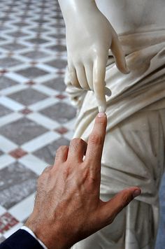 a hand reaching for something in front of a white statue with one hand on it's finger