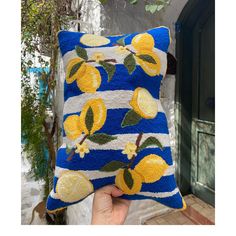 a hand holding a blue and yellow pillow with lemons printed on it in front of a doorway