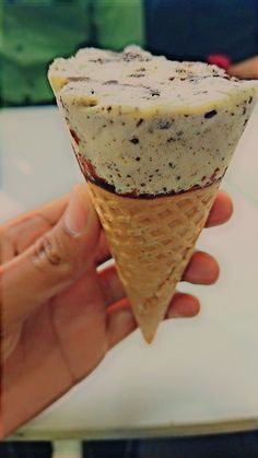 a hand holding an ice cream cone with chocolate chip toppings in it's cone