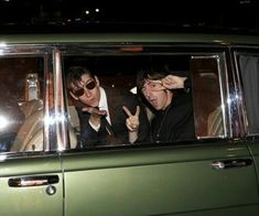 three people sitting in the passenger seat of a green car with their hands up to their ears