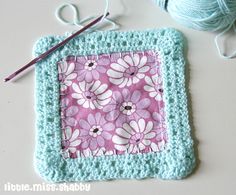 there is a crochet square with flowers on it next to yarn and knitting needles