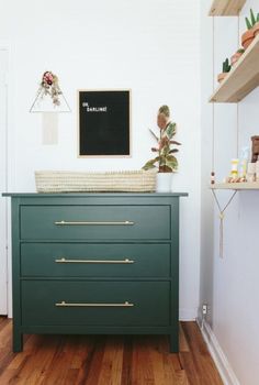 a green dresser in a white room with wooden floors and shelving on the wall