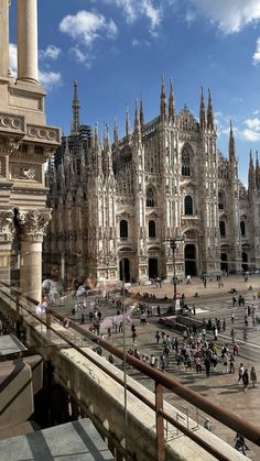 many people are walking around in front of an old building with tall towers and spires