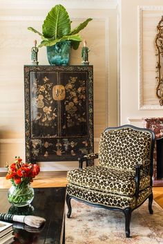 a leopard print chair sitting in front of a black cabinet with a green plant on top