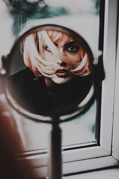 a woman looking through a magnifying glass with her face reflected in the mirror