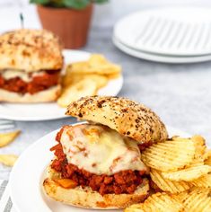 two plates with sandwiches and chips on them