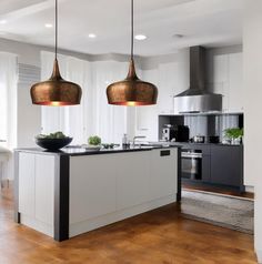 two lights hanging over a kitchen island in a room with hardwood floors and white walls