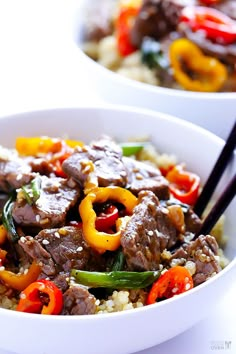 a white bowl filled with beef and peppers on top of rice topped with chopsticks