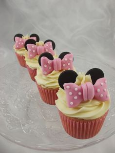 three cupcakes with pink and white bows are on a clear plate, ready to be eaten