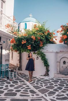 a woman standing in front of a white building with orange flowers growing on the wall