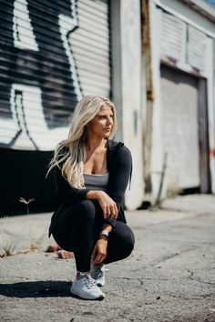 a woman squatting on the ground in front of a building with graffiti painted on it