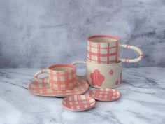 pink and white checkered coffee cups and saucers with matching plates on a marble surface