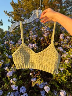 a woman's hand is holding up a bralet in front of some flowers