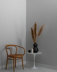 a chair next to a table with a vase on it and a plant in the corner