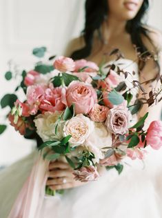 a woman holding a bouquet of flowers in her hands and wearing a wedding dress with pink ribbons