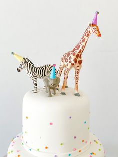 two giraffes and a zebra on top of a white cake with sprinkles