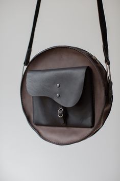 a black leather bag hanging from a hook on a wall with the strap down to it's shoulder