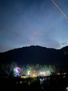 an amusement park lit up at night with ferris wheel in the foreground and mountains in the background