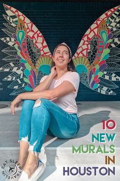 a woman sitting on the ground in front of a wall with an image of a butterfly painted on it