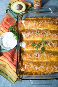 an enchilada casserole in a baking dish with sour cream on the side