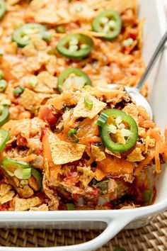 a casserole dish filled with nachos, cheese and jalapenos