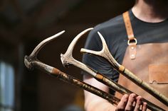 a man holding three deer antlers in his right hand and wearing an apron on the left