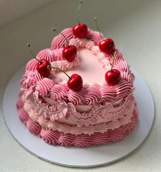 a cake with pink icing and cherries on top sitting on a white plate