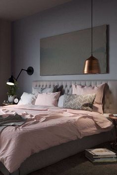 a bed with pink sheets and pillows in a bedroom next to a lamp on the wall