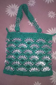 a green crocheted bag sitting on top of a pink bed cover with white flowers