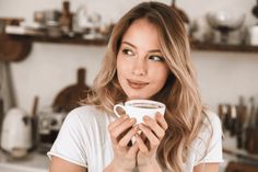 a woman holding a cup of coffee in front of her face and looking at the camera