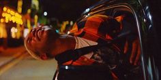 a man with his eyes closed leaning out the window of a car on a city street at night