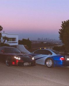 two cars parked next to each other in front of a building with the city skyline behind them