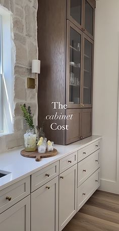 a kitchen with white cabinets and wood flooring next to a window that reads the cabinet cost