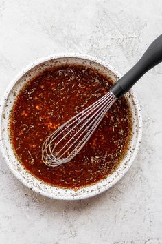 a bowl filled with sauce and whisk on top of a white countertop