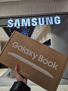 a person holding up a samsung book in front of a building with the words galaxy book on it